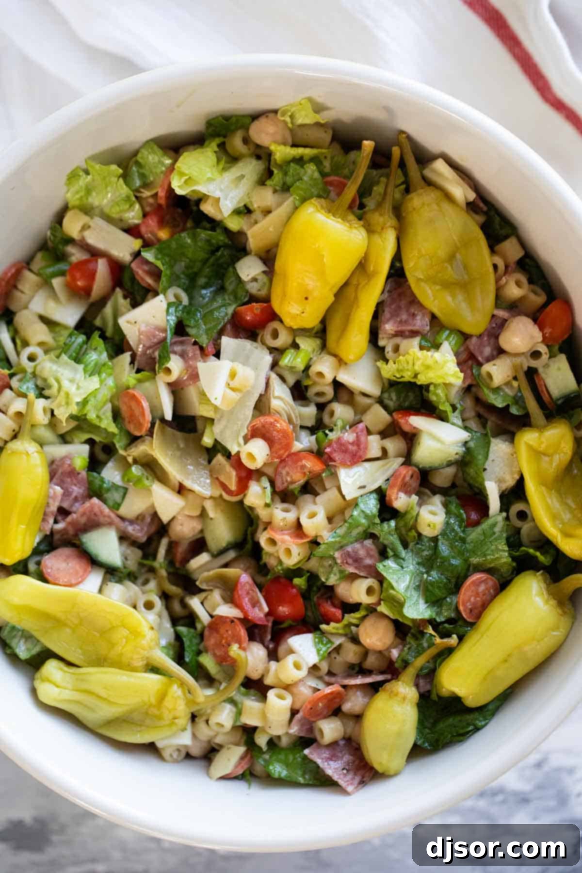 Italian Chopped Salad with Pasta, Meat, and Cheese A close-up shot of a vibrant Italian Chopped Salad featuring a rich mix of pasta, slices of salami, cubes of cheese, and fresh vegetables.