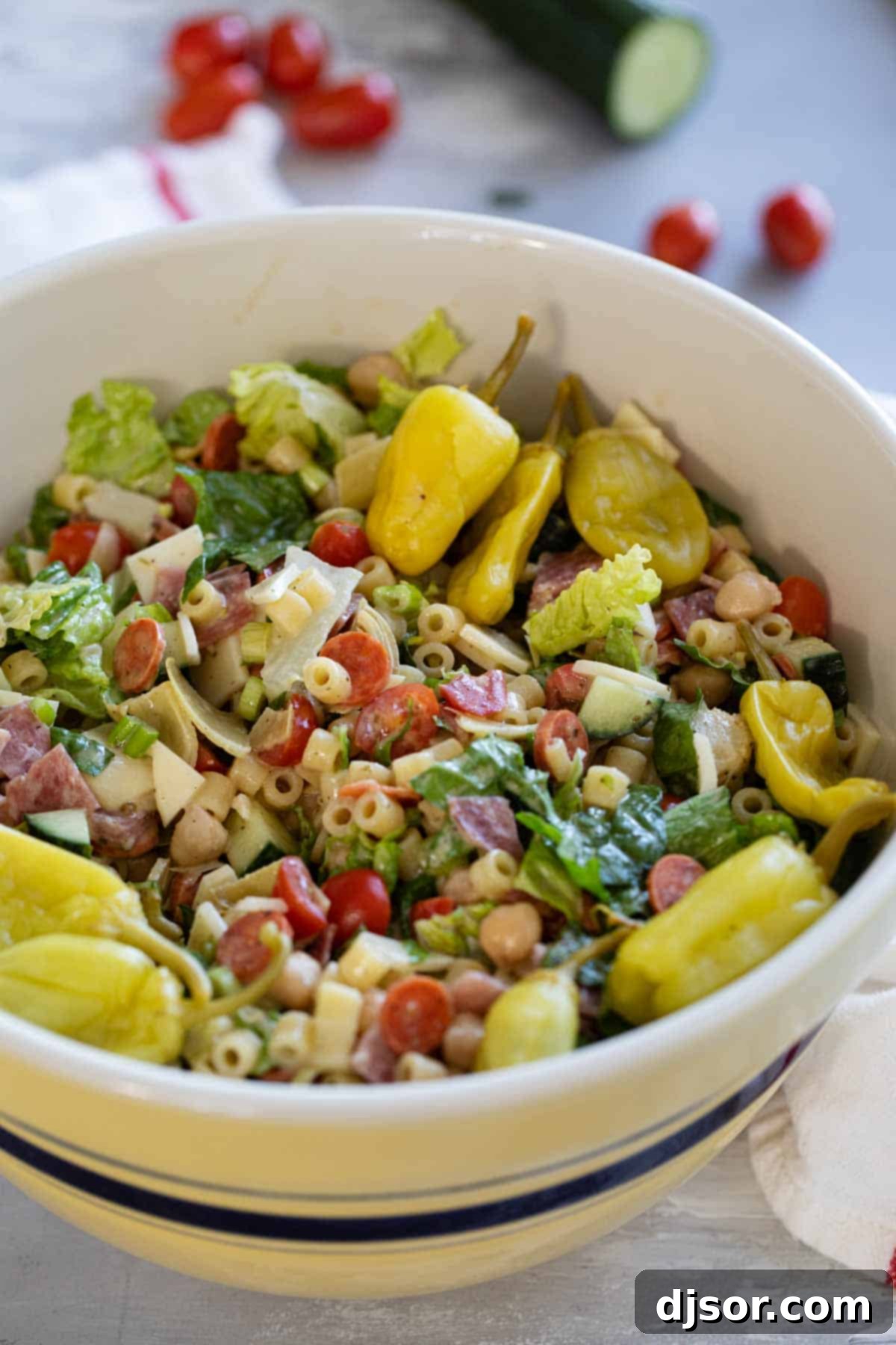 Flavorful and hearty, this Italian Chopped Salad has all of the great flavors of Italy in one huge salad! Filled with salami, cheese, vegetables, and so much more, then topped with and easy homemade dressing, this salad will become an instant favorite. A vibrant Italian Chopped Salad in a large glass bowl, topped generously with bright green pepperoncini peppers.