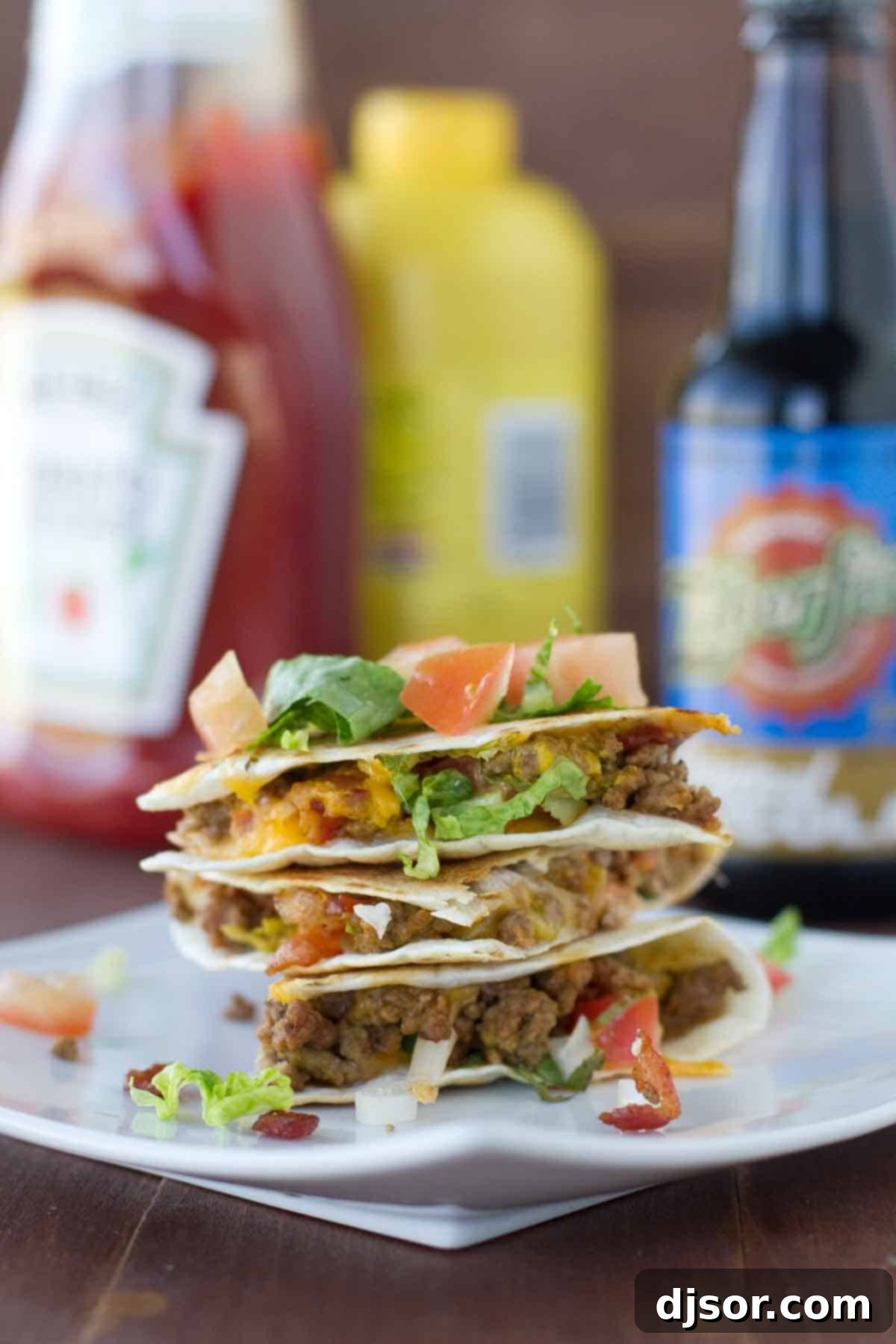 Two Bacon Cheeseburger Quesadillas stacked on a rustic plate, garnished with fresh lettuce and diced tomatoes, highlighting the crispy tortilla and melted cheese.