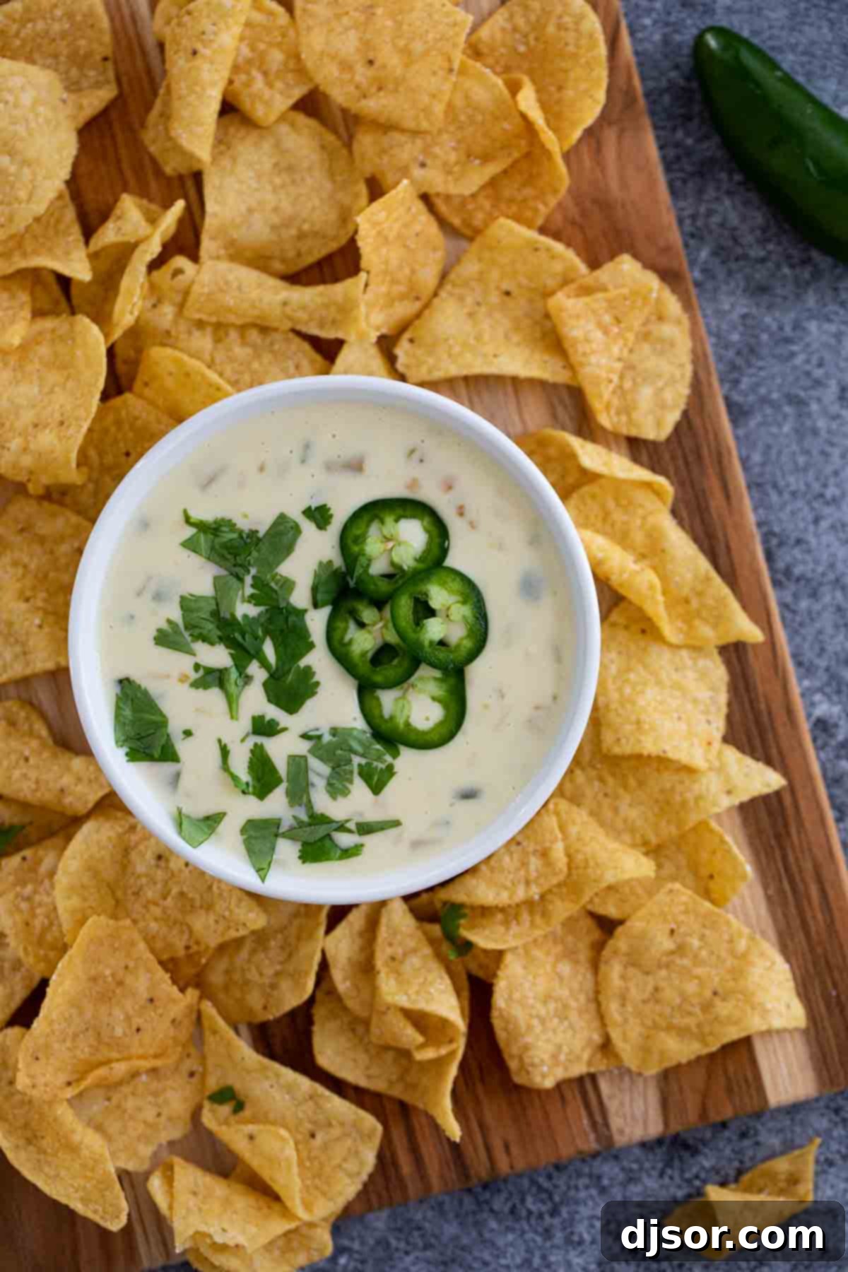 An overhead shot showcasing a vibrant bowl of Queso Blanco, adorned with sliced green jalapeños and fresh cilantro, flanked by a generous pile of crispy tortilla chips.