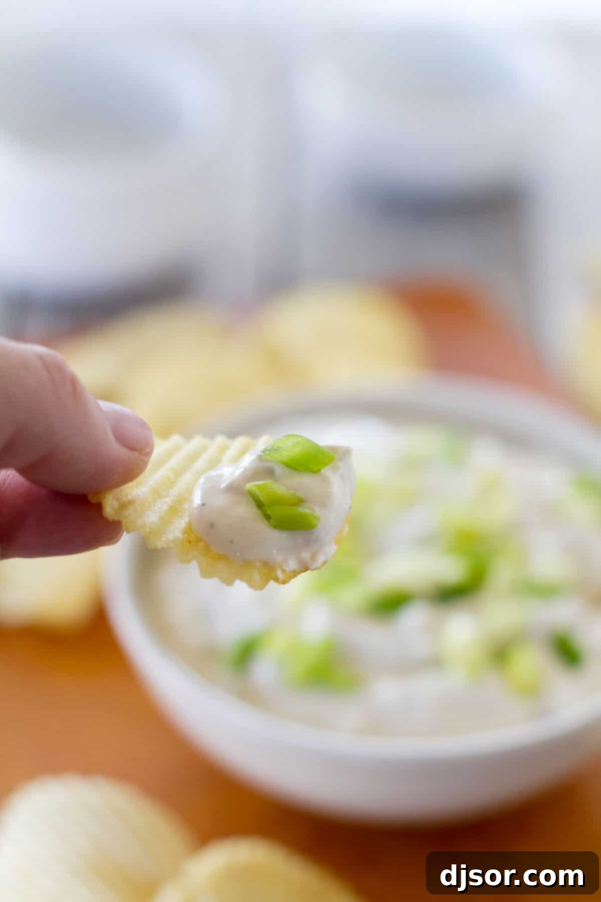 Potato Chip with Bacon Horseradish Dip A hand holding a potato chip loaded with homemade Bacon Horseradish Dip, showcasing its rich texture and irresistible appeal.