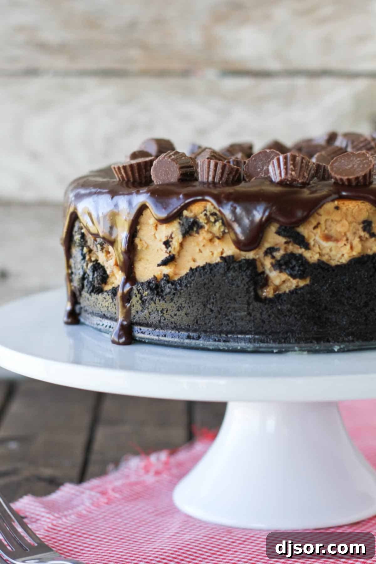 A full, tall Reese's Peanut Butter Cheesecake sitting on a elegant cake stand, ready to be sliced and served.