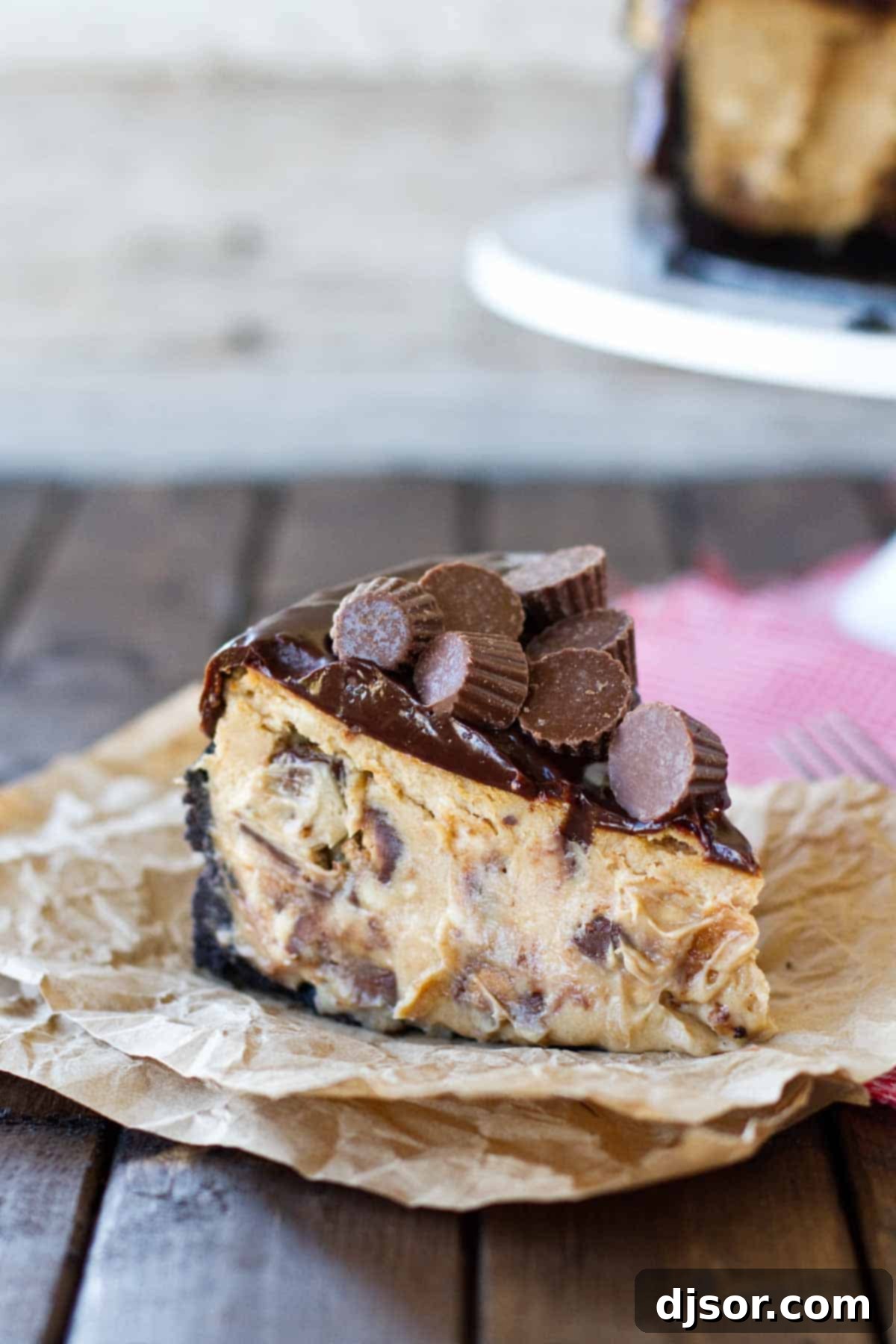 A perfectly sliced piece of Reese's Peanut Butter Cheesecake, showing off its layers of cookie crust, peanut butter filling with candy pieces, and chocolate ganache.