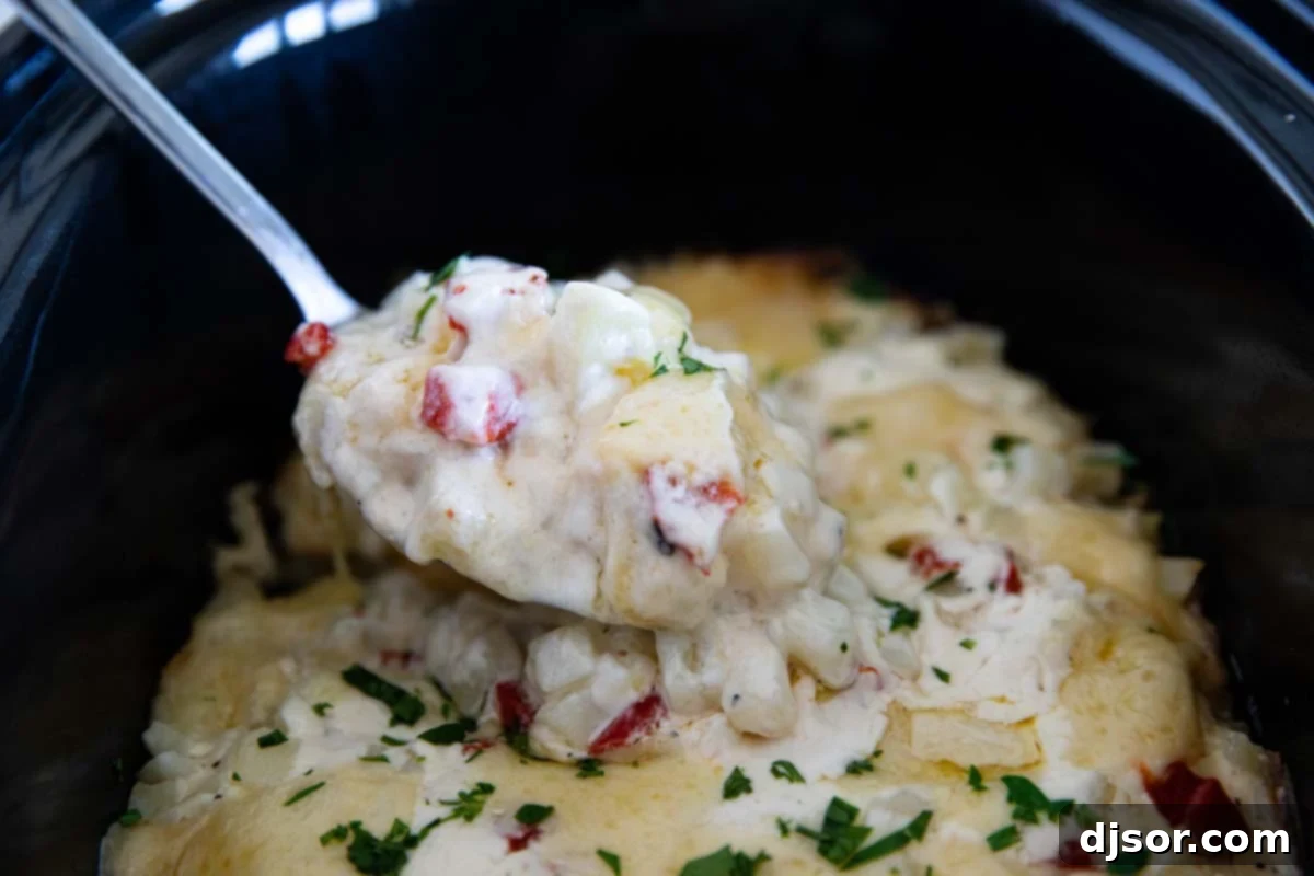A serving spoon scooping out a portion of perfectly cooked, cheesy potatoes from a slow cooker.