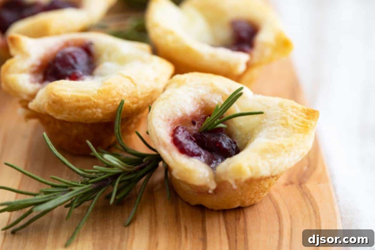 Elegant Cranberry Brie Bites garnished with fresh rosemary on a wooden cutting board, ideal for holiday appetizers.