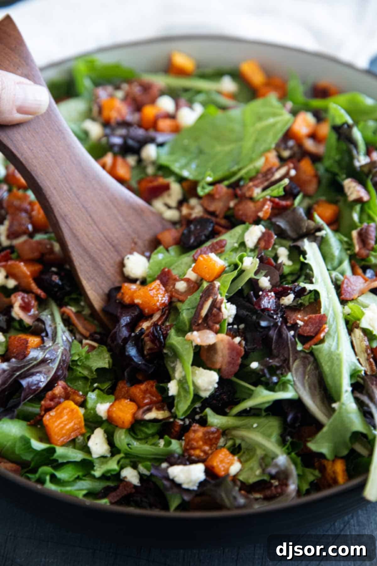 Autumn Harvest Medley 7 A pair of salad spoons gracefully dishing out a generous portion of Fall Harvest Salad from a large bowl, highlighting its abundant ingredients.