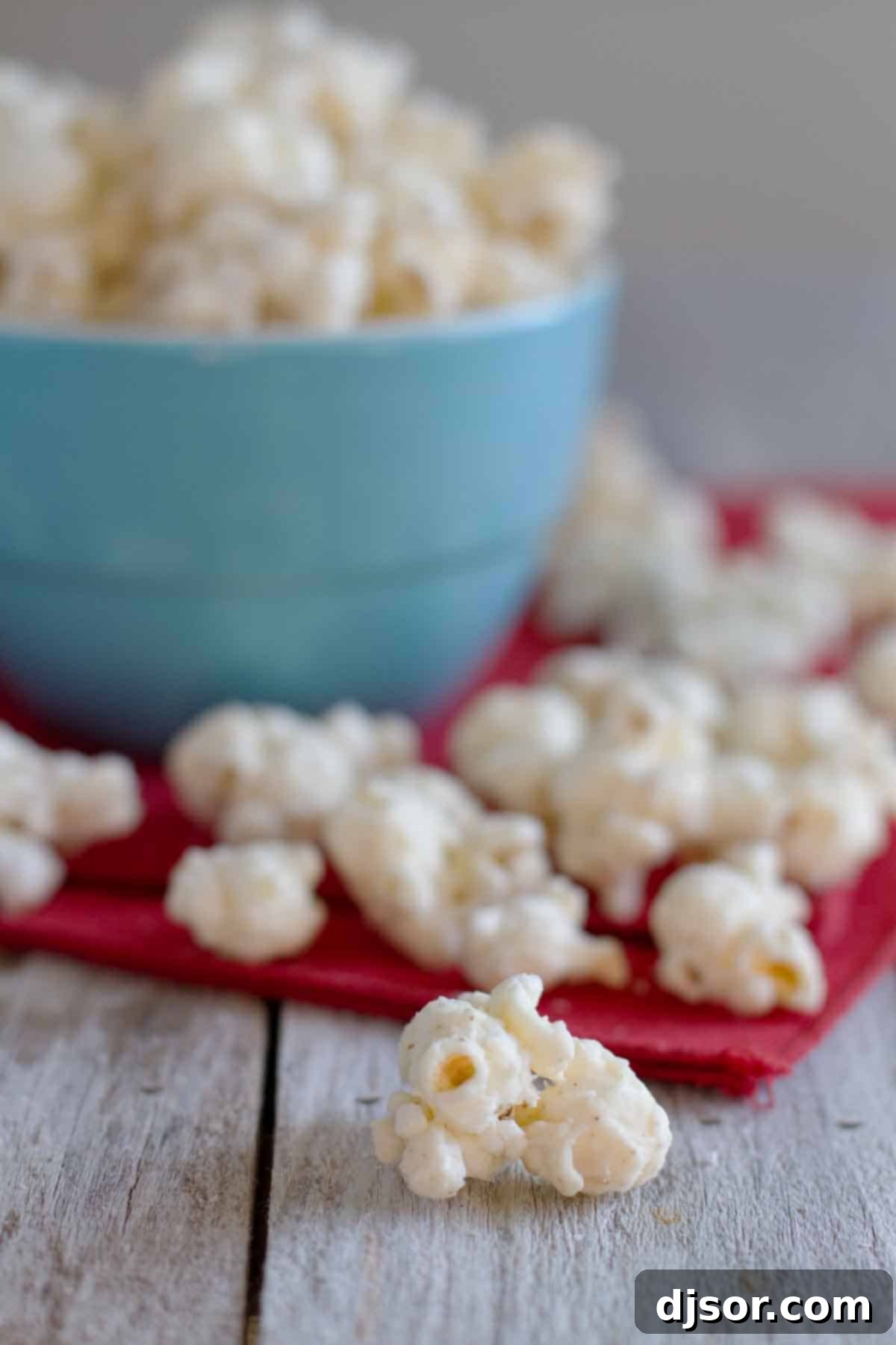 Close-up of Eggnog Popcorn pieces scattered next to a blue bowl, highlighting its crunchy texture.