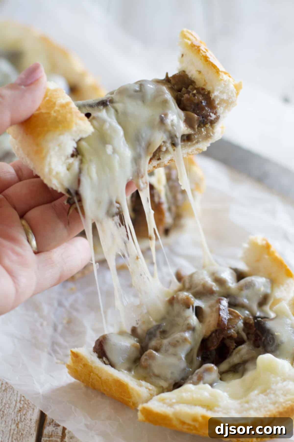 Gourmet Sausage and Portobello French Bread Pizza 3 Close-up of a cheese pull on a slice of French Bread Pizza with Sausage and Portobello Mushrooms, showcasing the gooey melted cheese.