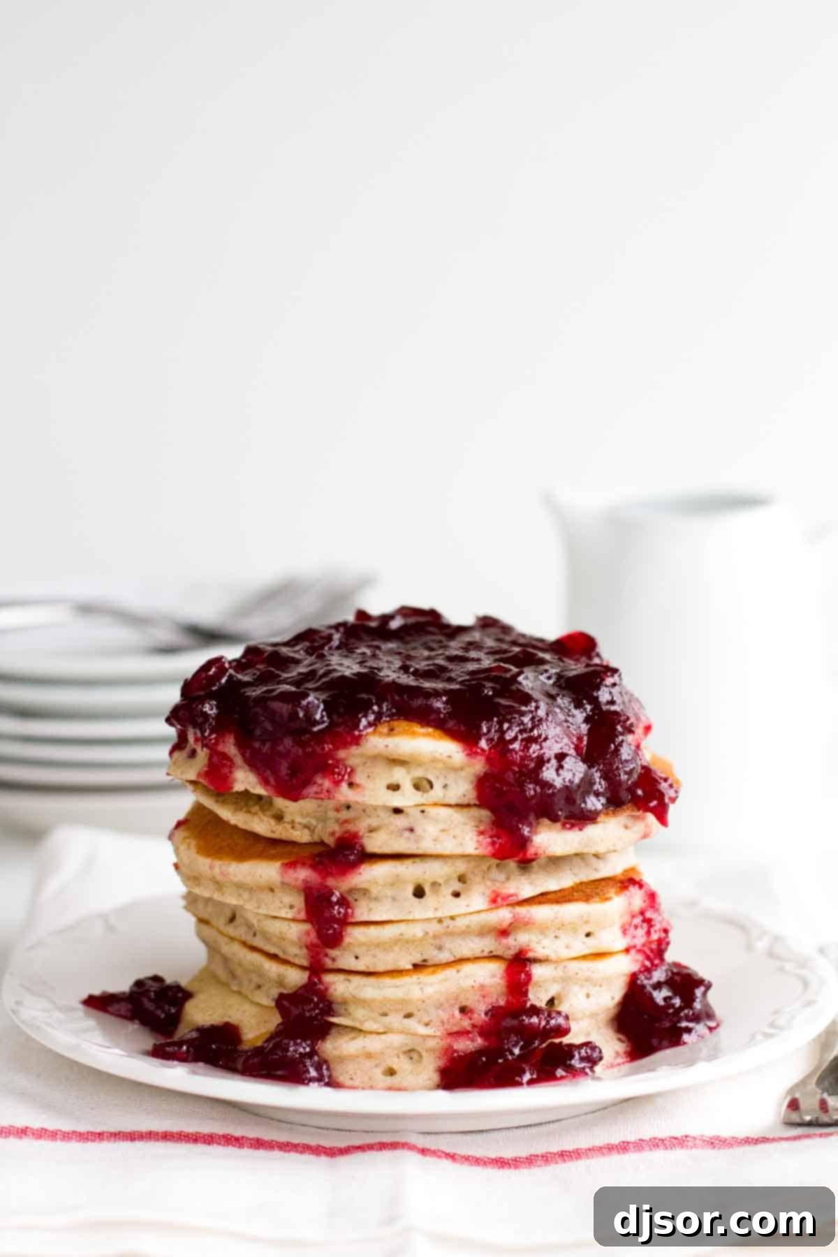 Tangy Cranberry Cloud Cakes 2 Stack of fluffy Cranberry Pancakes on a white plate, ready to be served, with a festive background hinting at winter mornings.