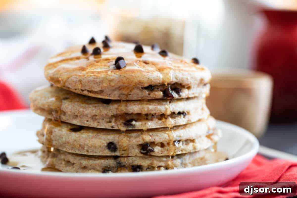 An easy recipe for a healthier breakfast choice, these Oatmeal Pancakes with Chocolate Chips are made with oats, whole wheat, and the perfect touch of sweetness from mini chocolate chips. stack of oatmeal pancakes with chocolate chips drizzled with syrup