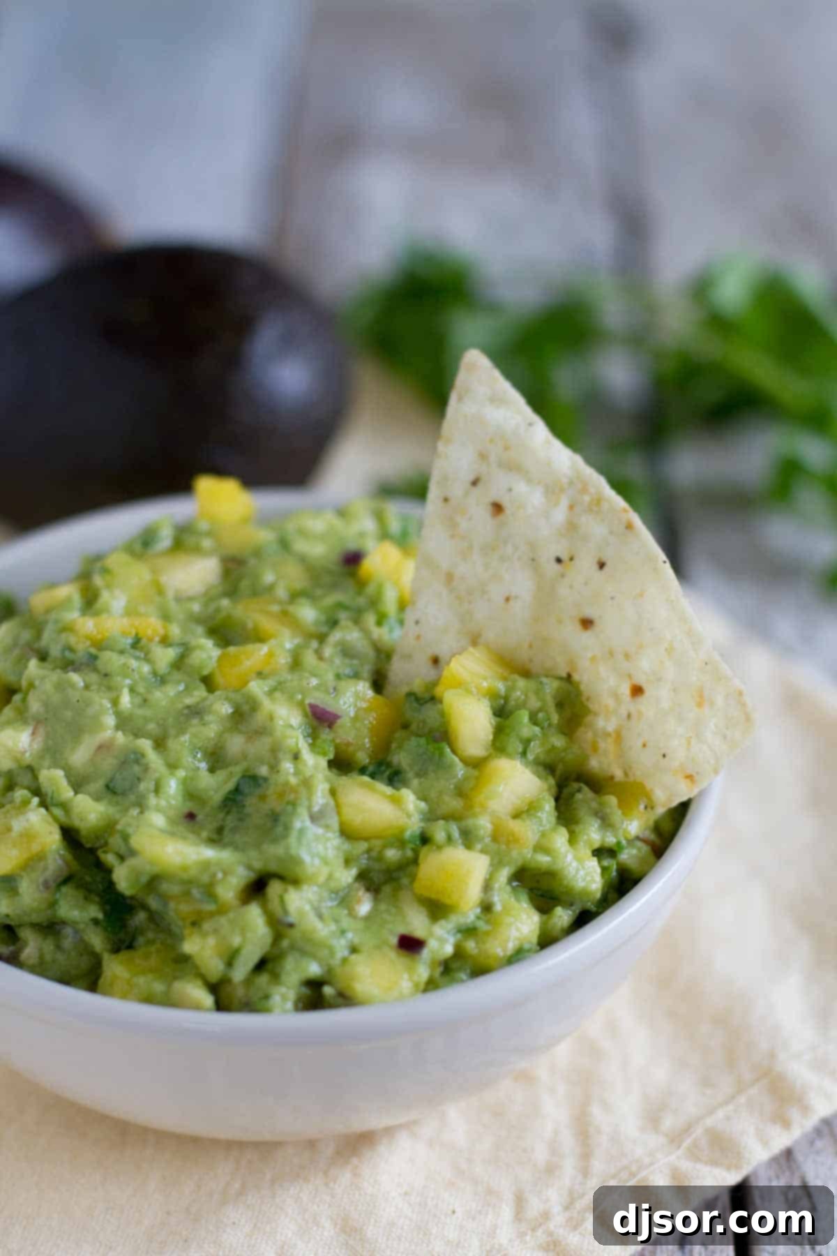 A taste of the tropics meets Mexico in this twist on guacamole in this Tropical Guacamole, loaded with Avocados from Mexico, Pineapple and Mango. Bowl filled with Tropical Guacamole with a tortilla chip.