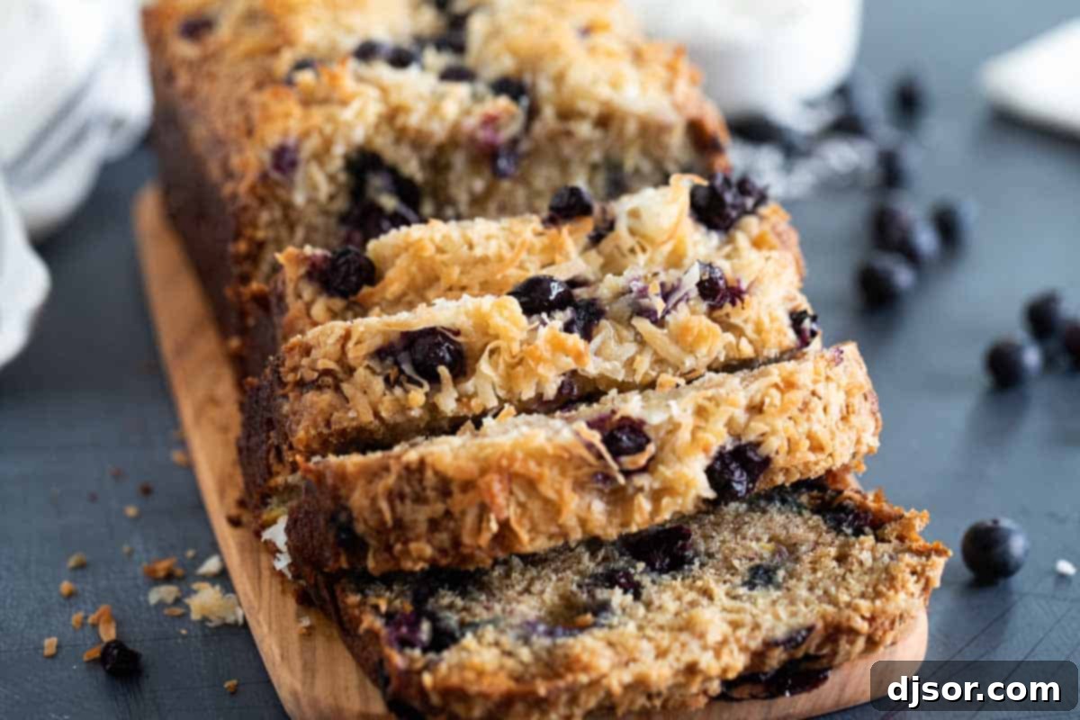 Make a change from your typical banana bread with this Blueberry Banana Bread with Coconut that is filled with fresh berries and topped with a crunchy streusel topping. A beautifully sliced loaf of blueberry banana bread with coconut, showcasing the vibrant berries and moist texture, rests on a rustic wooden cutting board, inviting a delightful taste.