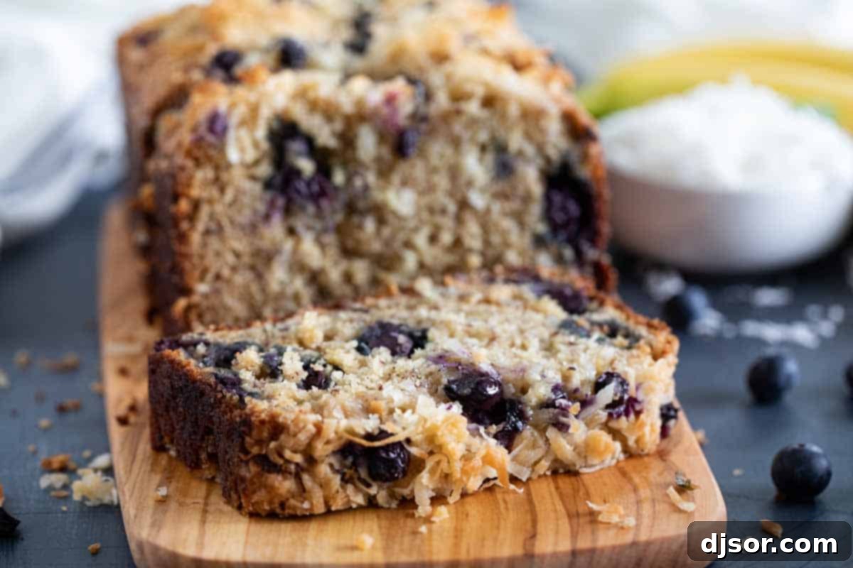 Make a change from your typical banana bread with this Blueberry Banana Bread with Coconut that is filled with fresh berries and topped with a crunchy streusel topping. A close-up shot revealing the beautiful, moist texture of a slice of blueberry banana bread with coconut, highlighting the tender crumb and distribution of fruit and coconut flakes.