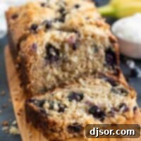Moist Blueberry Banana Bread with Toasted Coconut 2 A slice of blueberry banana bread with coconut on a cutting board, highlighting the moist texture and fruit distribution.