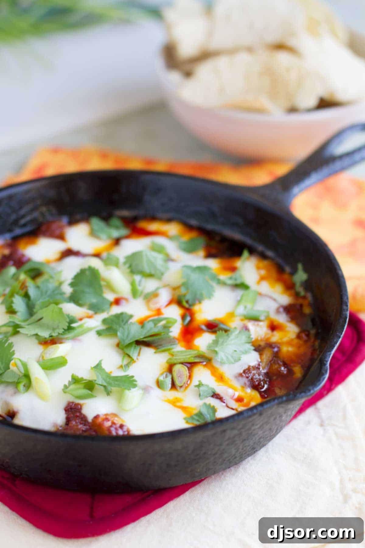 A cast iron skillet filled with a bubbling, golden Mushroom and Chorizo Queso Dip, generously topped with fresh green onions and cilantro, ready to be scooped with tortilla chips.