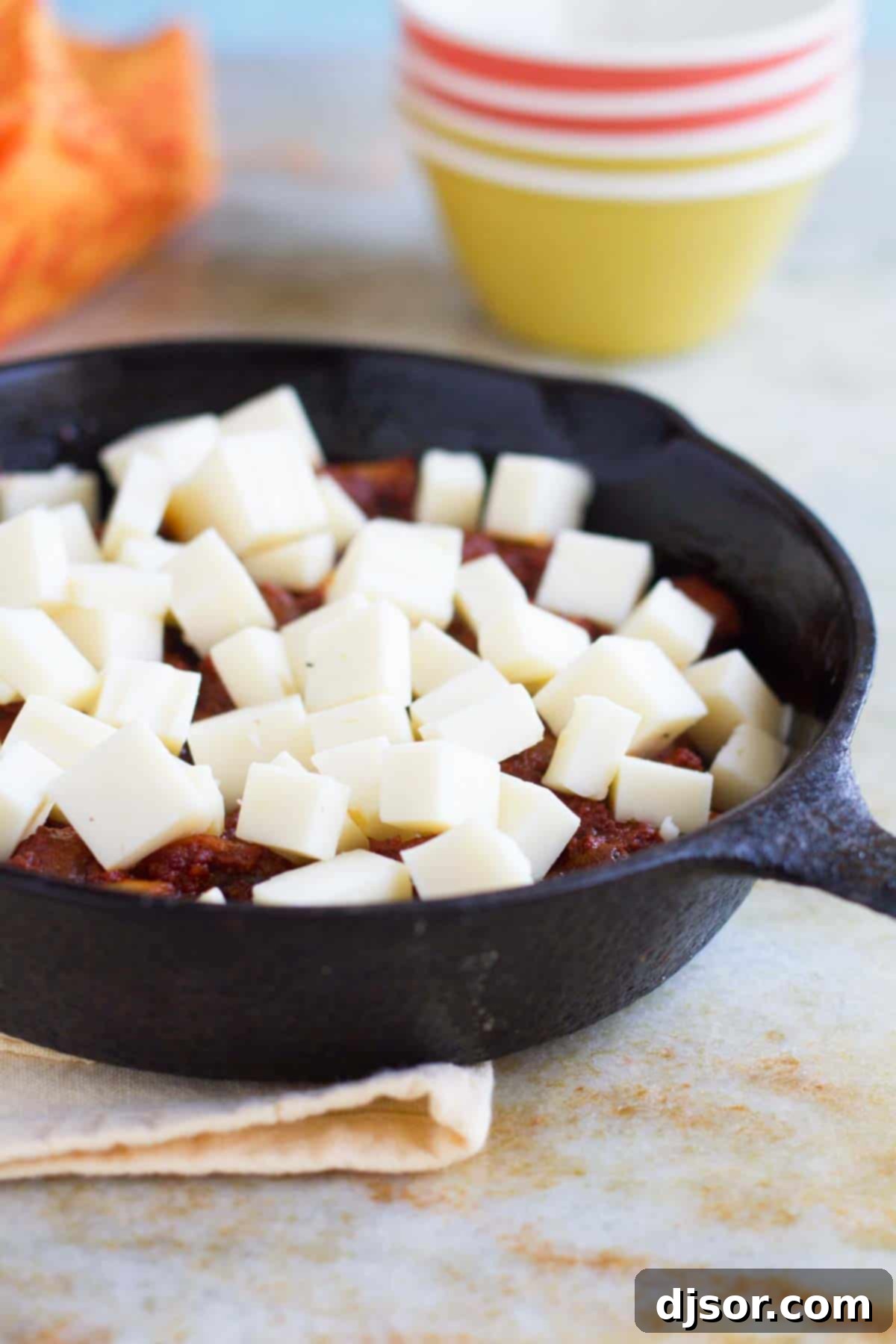 Close-up view of cubed Monterey Jack cheese melting over a bed of cooked chorizo and sautéed mushrooms in a cast iron skillet.