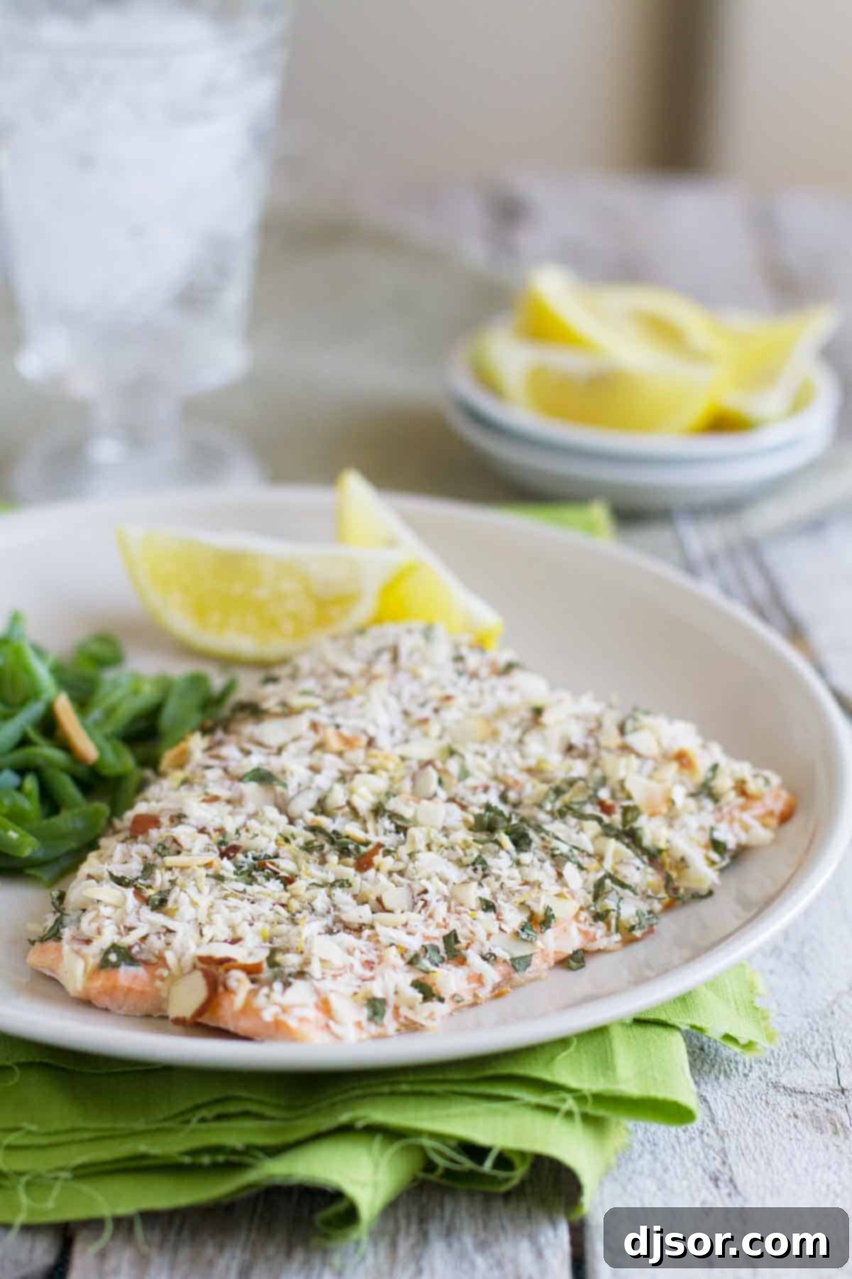 Baked salmon fillet coated with a golden almond and herb crust, served with fresh lemon slices on a plate.