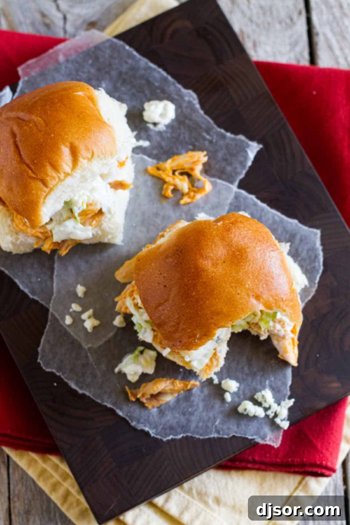 Close-up of a buffalo chicken sandwich with a bite taken out, showing the layers of spicy chicken and creamy blue cheese slaw on a soft bun.