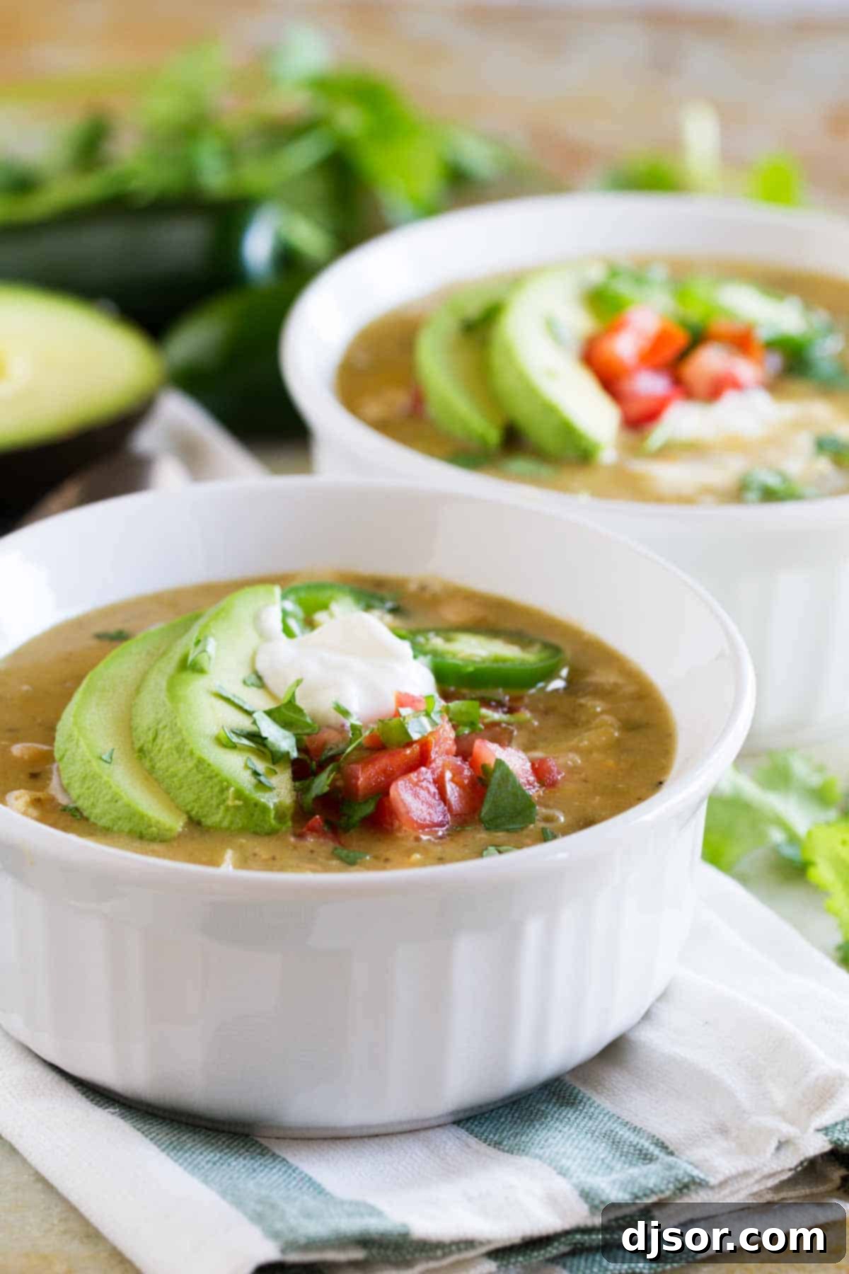Two bowls of spicy White Chicken Chili garnished with fresh cilantro and a dollop of sour cream, on a rustic wooden surface.