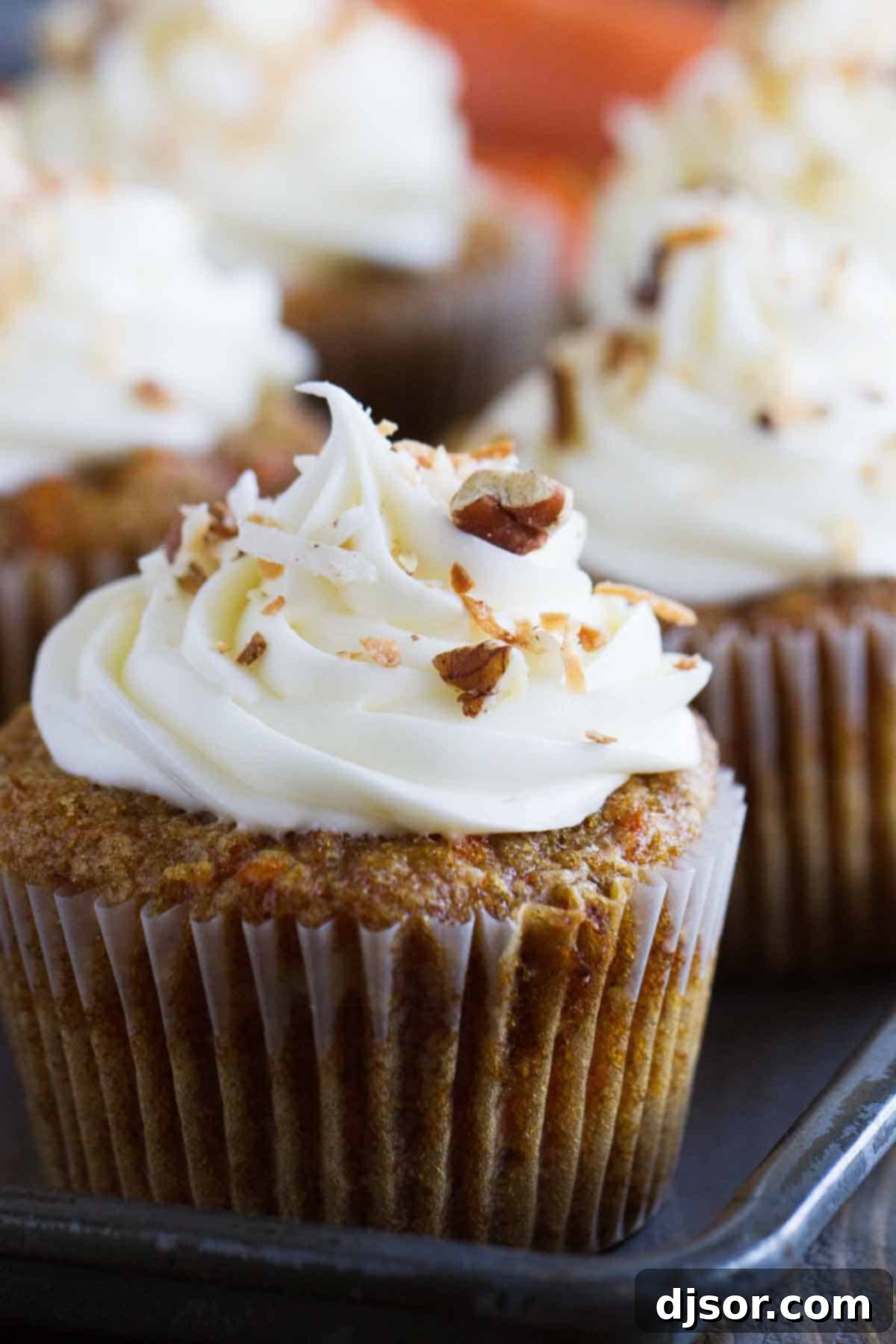 close up of carrot cake cupcake topped with cream cheese frosting, nuts, and coconut