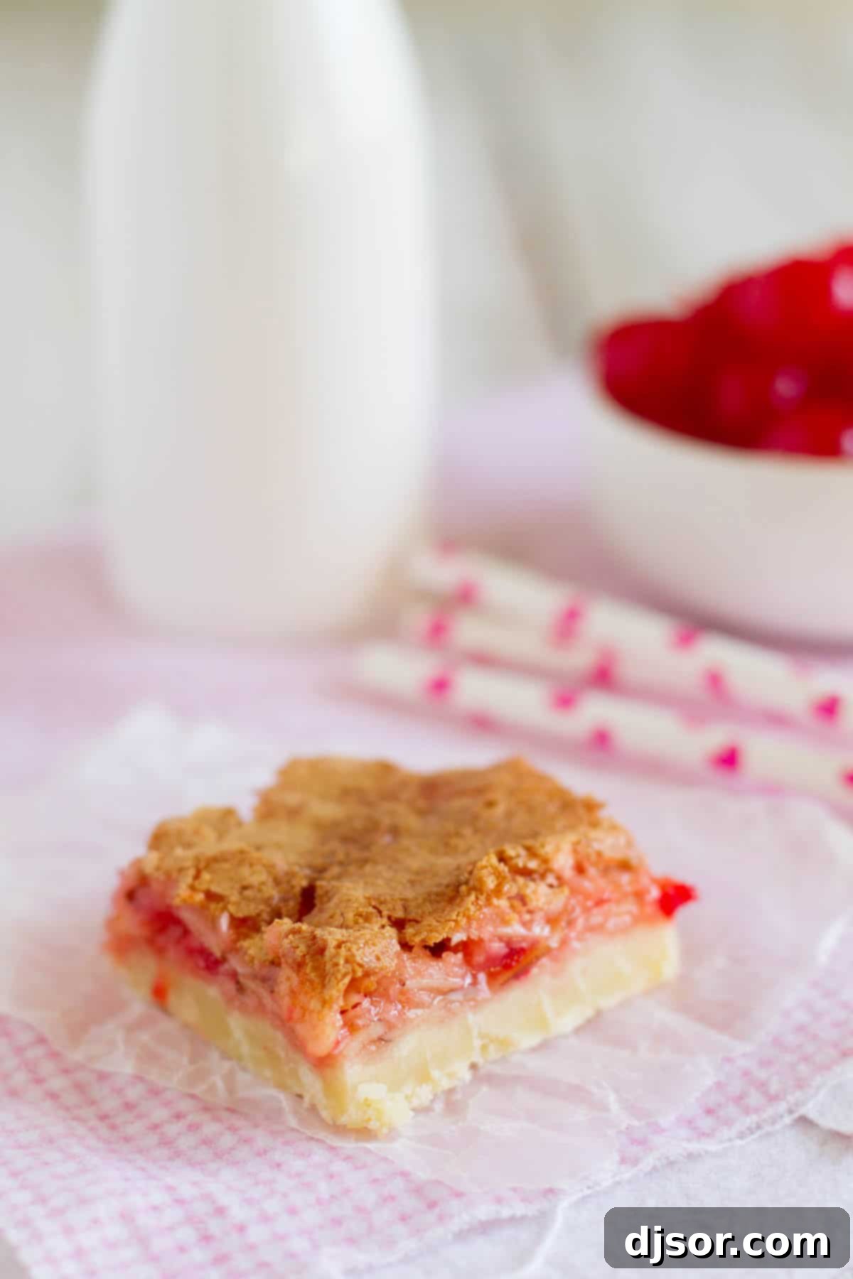 A delectable Coconut Cherry Almond Bar resting on soft pink fabric, showcasing its sweet, gooey layers perfect for a special treat.