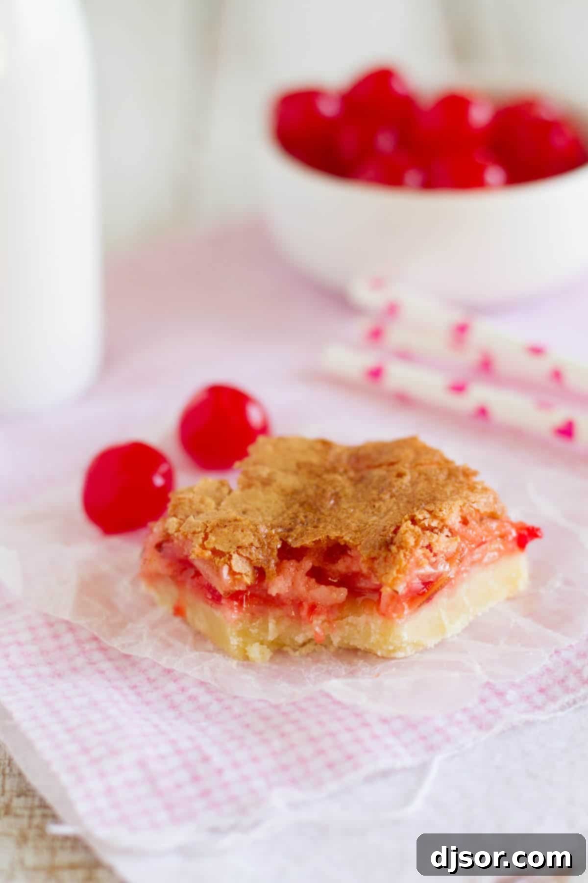 A close-up of a Coconut Cherry Almond Bar with a bite taken out, revealing its soft, chewy interior and vibrant cherry pieces.