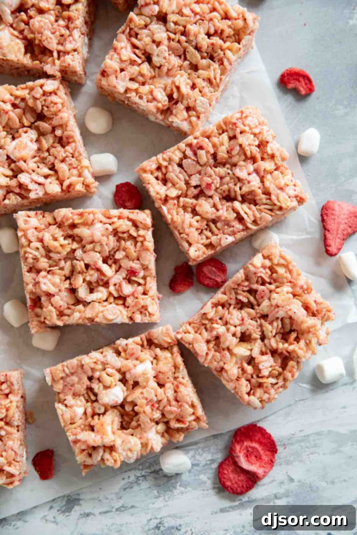 Delicious Strawberry Rice Krispie Treats cut into bars, garnished with freeze-dried strawberries and miniature marshmallows, arranged on a rustic surface.