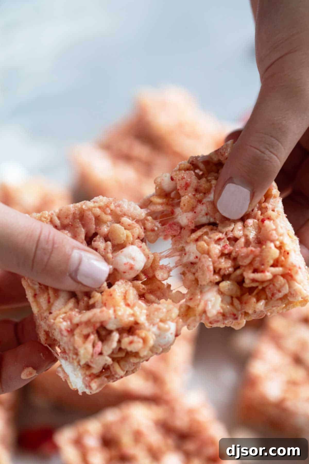 Pink Strawberry Crispy Treats 10 Hands gently pulling apart a Strawberry Rice Krispie Treat, showcasing its incredibly soft, gooey, and chewy texture.