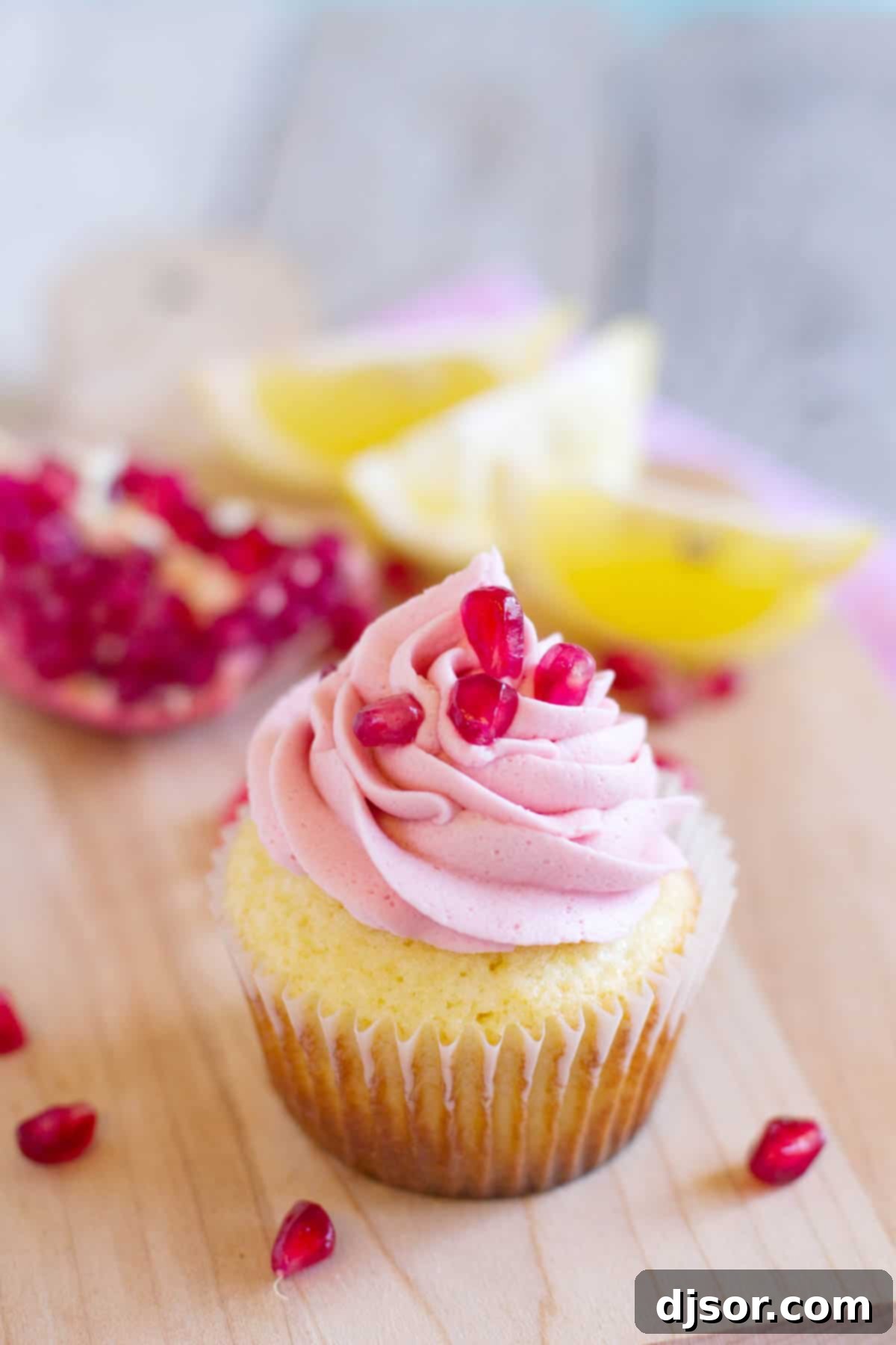 Close-up of a single Lemon Pomegranate Cupcake with a fresh pomegranate in the background.