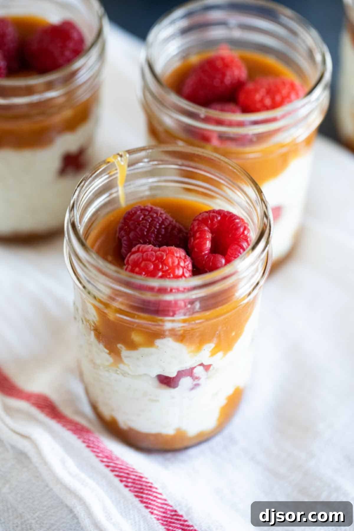 Jars filled with beautifully layered rice pudding, rich caramel, and vibrant fresh raspberries, ready to serve.