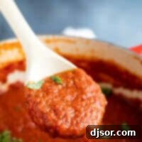 A wooden spoon lifted from a pot, showcasing a generous scoop of homemade marinara sauce, garnished with a sprinkle of fresh basil.