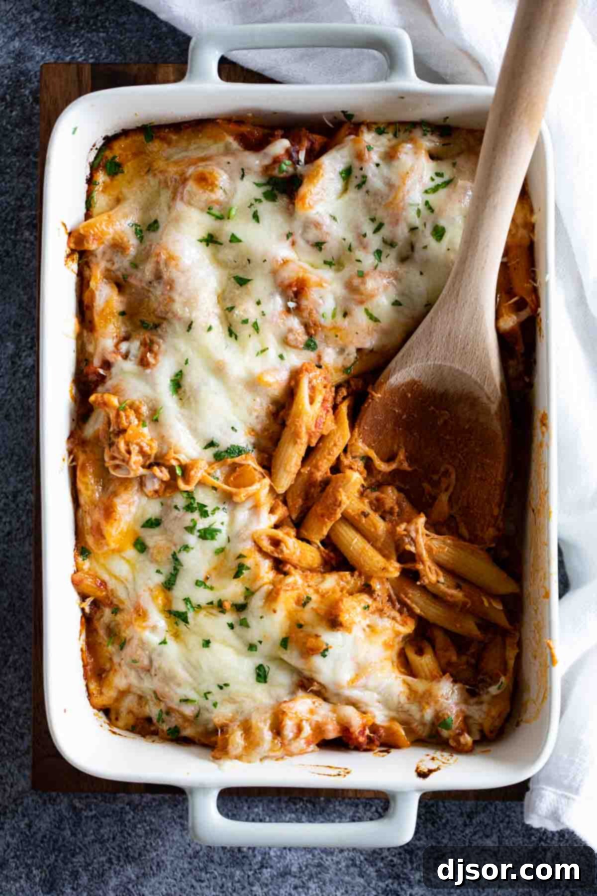 Pure comfort food, this Penne Pasta Bake recipe has a meaty, creamy sauce and lots and lots of cheese. It is perfect for a busy night, and is perfect for feeding a crowd. overhead view of Penne Pasta Bake recipe with wooden serving spoon