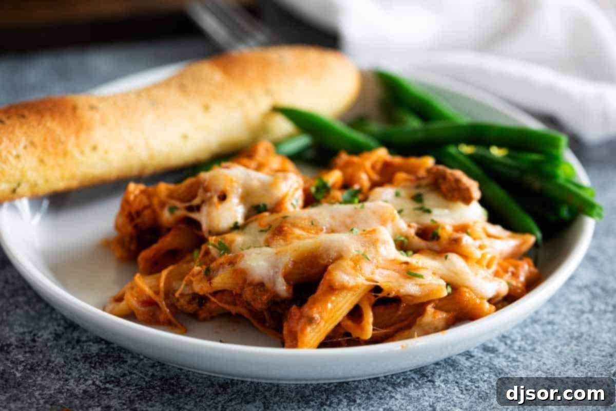 Pure comfort food, this Penne Pasta Bake recipe has a meaty, creamy sauce and lots and lots of cheese. It is perfect for a busy night, and is perfect for feeding a crowd. plate with penne pasta bake, green beans and breadstick