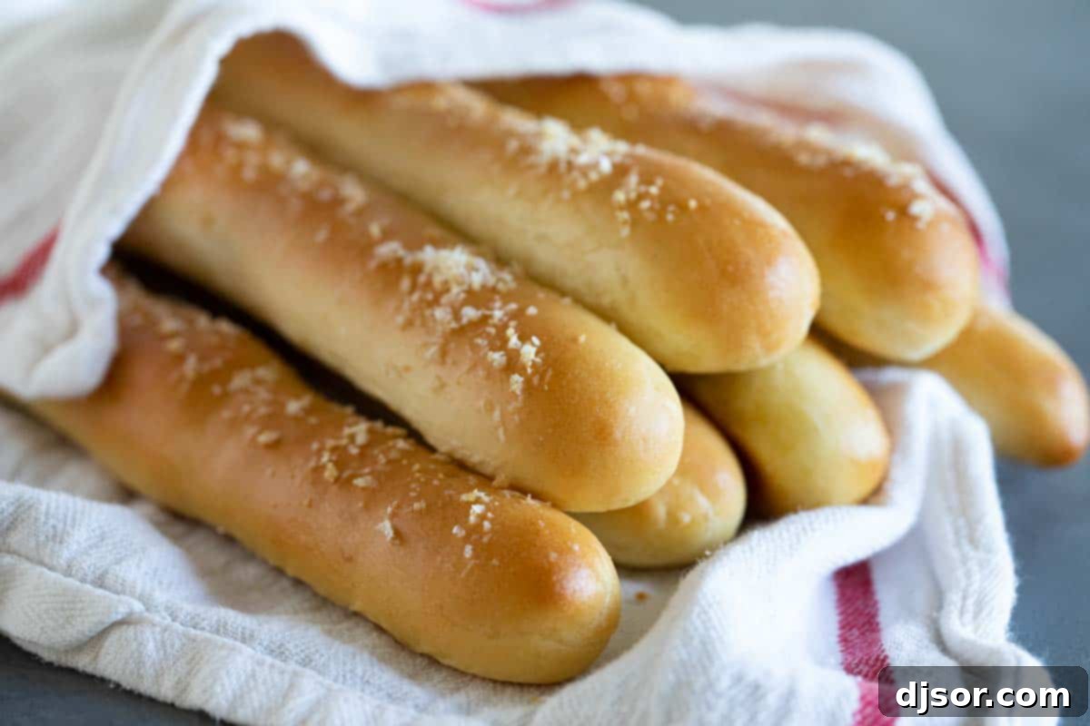 Freshly baked homemade breadsticks wrapped in a soft kitchen towel, exuding warmth and comfort.