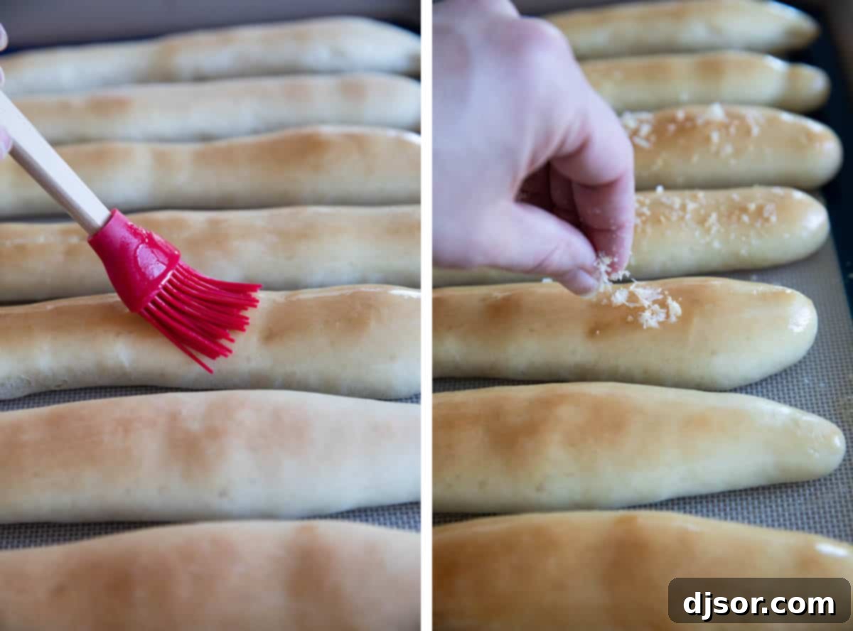 A close-up shot of baked breadsticks being brushed with melted butter and sprinkled with Parmesan cheese and garlic powder.
