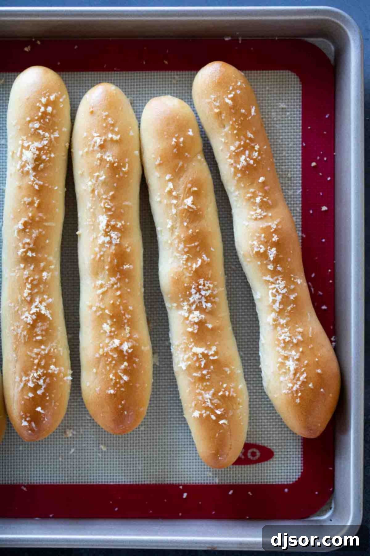 Freshly baked golden-brown breadsticks arranged neatly on a baking sheet, ready to be served.