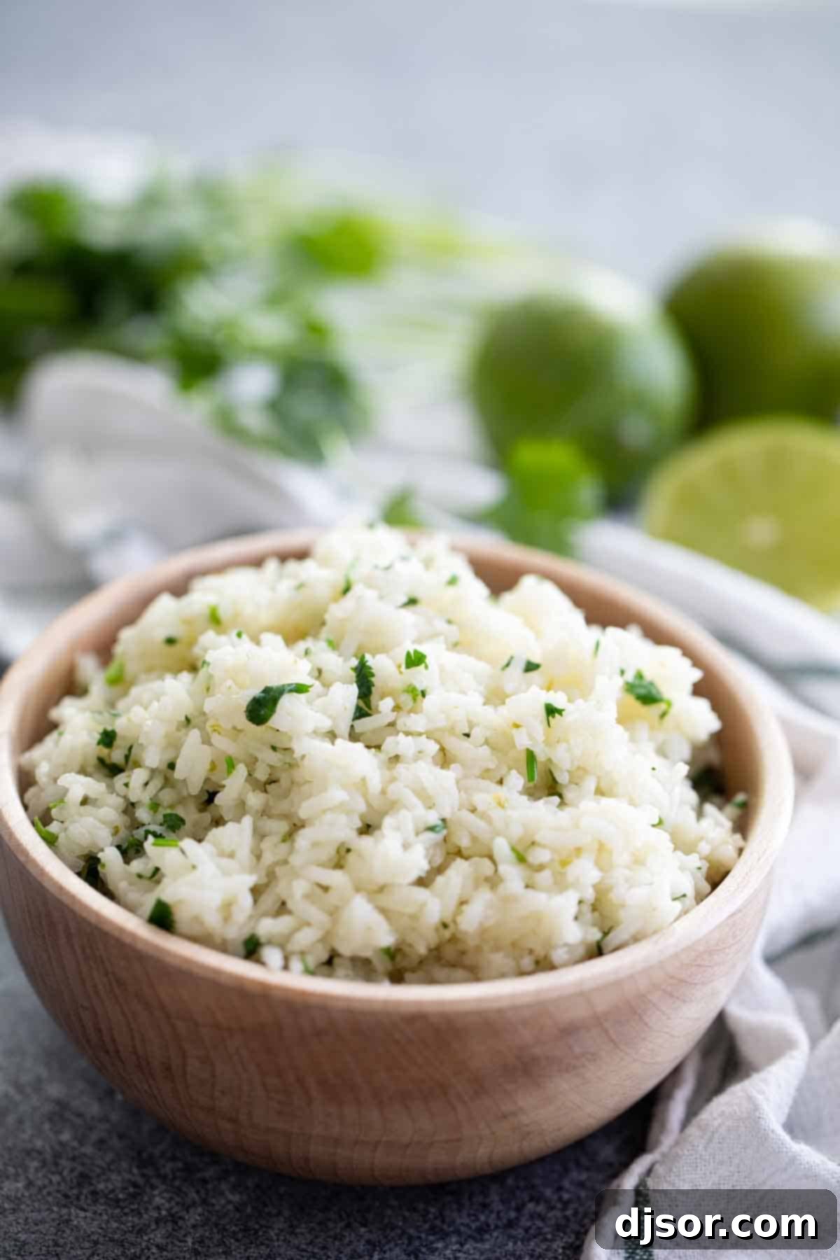A wooden bowl filled with freshly made Cilantro Lime Rice, garnished with fresh lime wedges, showcasing its vibrant appeal.