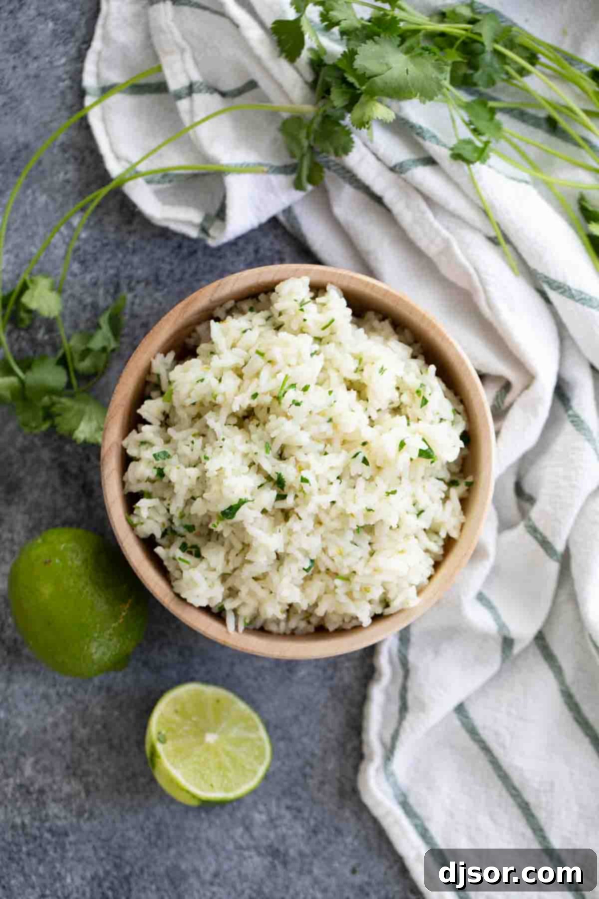 An overhead view of a rustic wooden bowl filled with fluffy Cilantro Lime Rice, highlighting its texture and fresh green cilantro flecks.