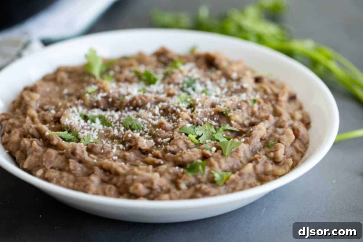 A beautiful bowl of homemade refried beans, elegantly topped with fresh cilantro and a sprinkle of cotija cheese, ready to be enjoyed.