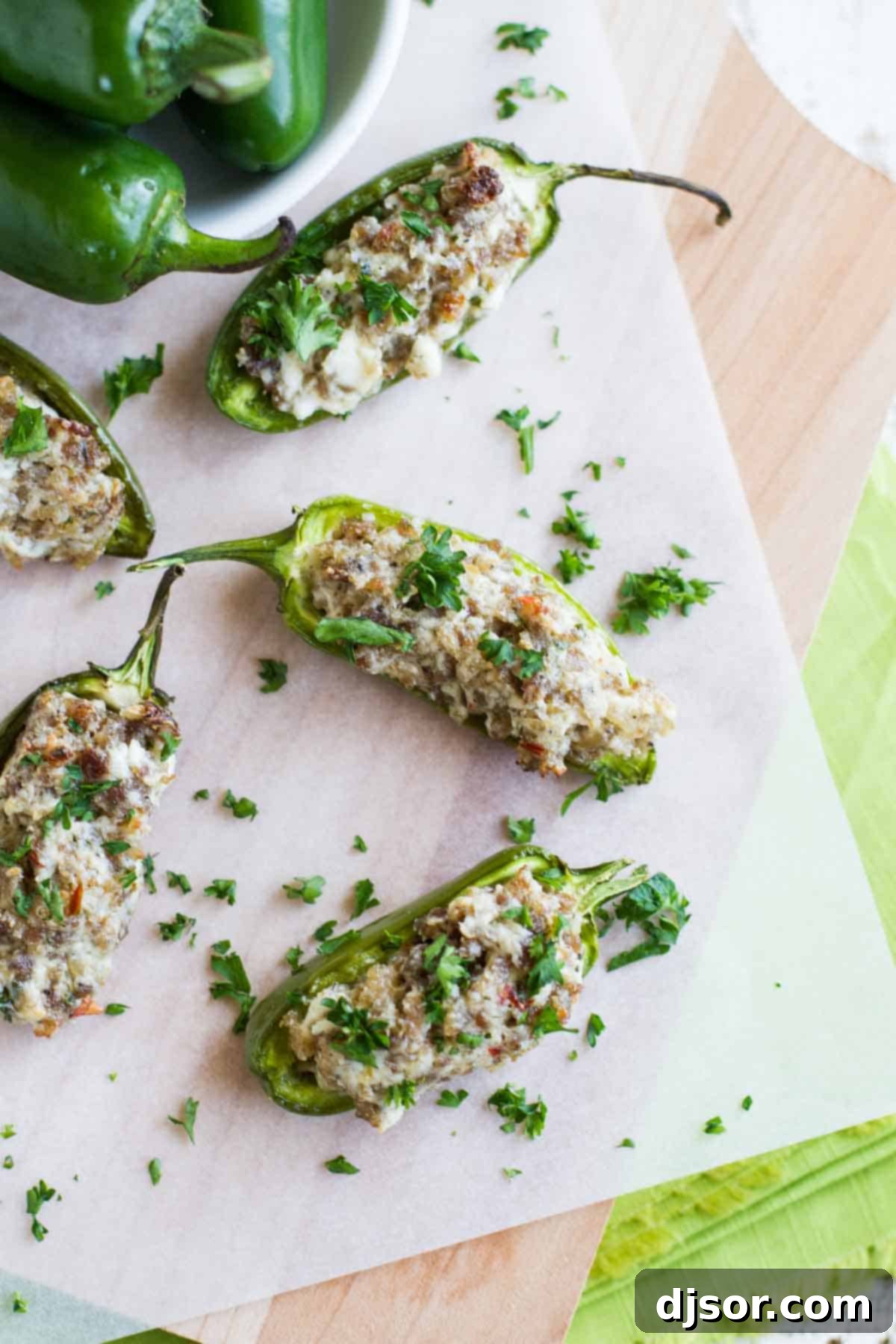These Sausage Stuffed Jalapeños are the perfect appetizer - jalapeño halves that are filled with a sausage and cheese mixture for a cheesy and spicy appetizer bite. Perfect for game day or for company. Sausage stuffed jalapeños on parchment paper.