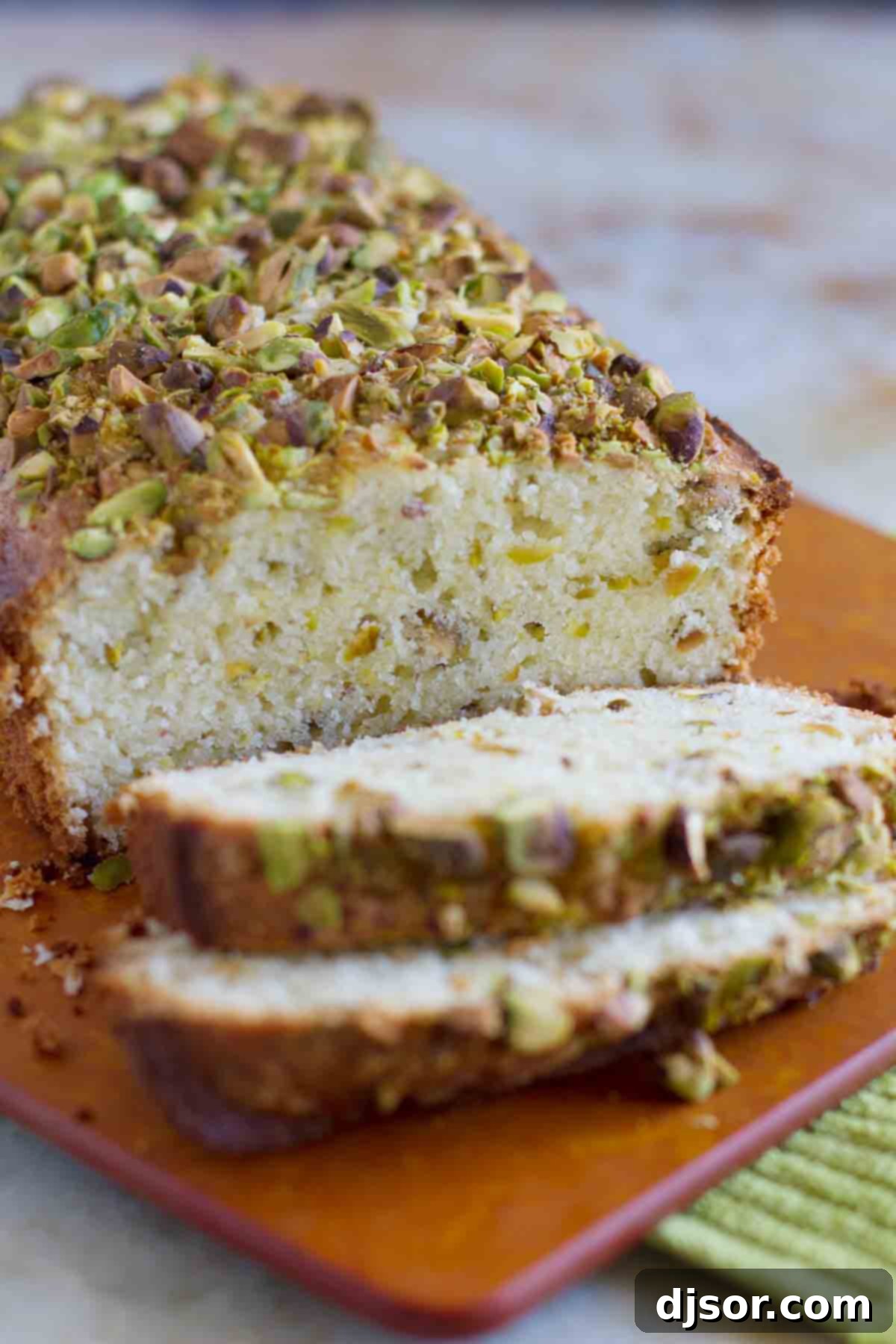 A beautifully baked loaf of Pistachio Lemon Pound Cake with two inviting slices on a wooden board, ready to be enjoyed.