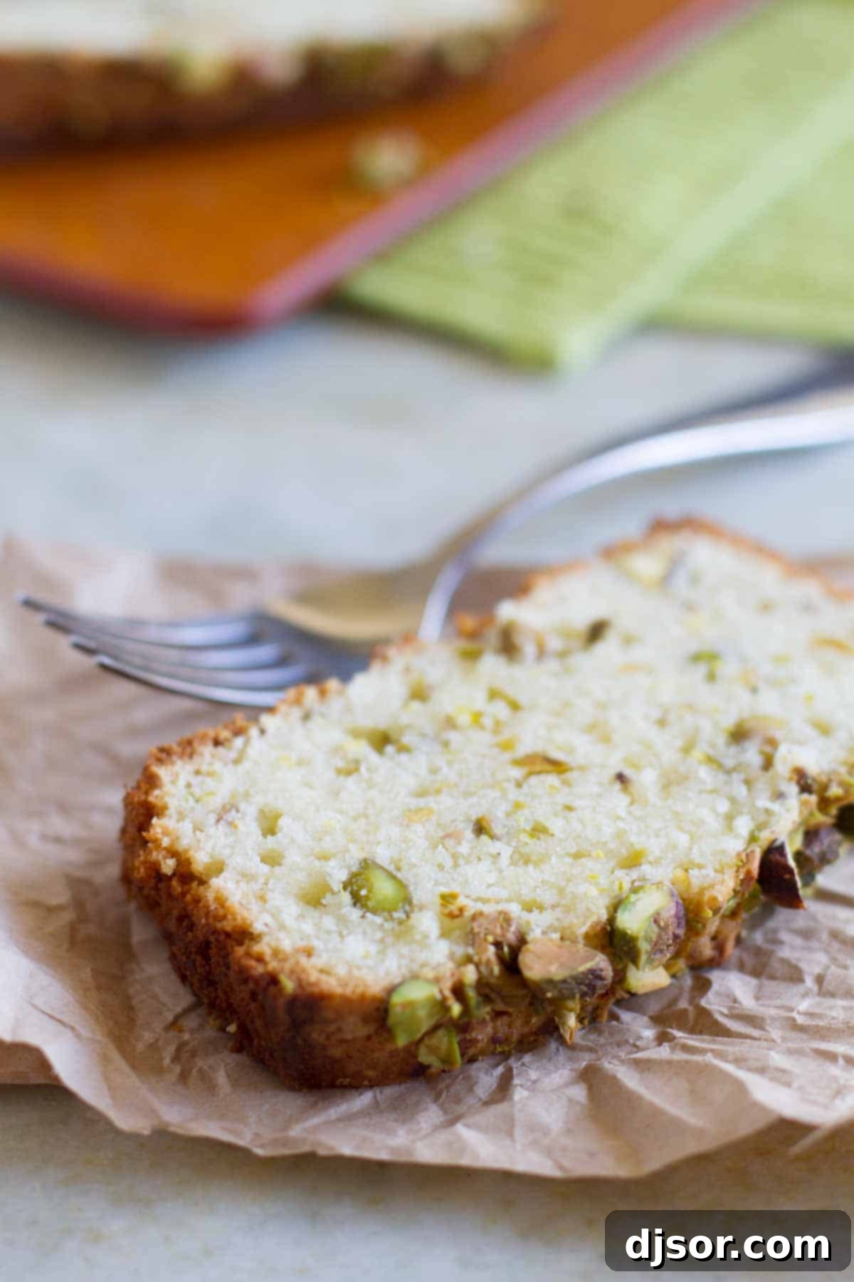 A perfectly sliced piece of Pistachio Lemon Pound Cake resting on rustic brown parchment paper, showcasing its moist texture and vibrant green pistachio bits.