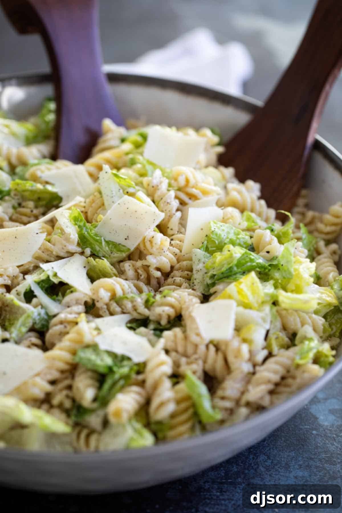 Bowl of Caesar Salad with Pasta with salad tongs, ready to be served.