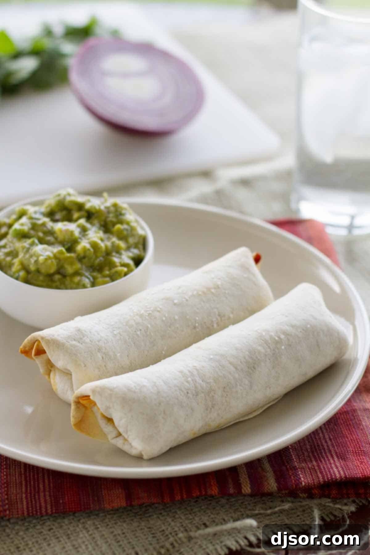 A close-up of two perfectly baked Mexican Egg Rolls, golden brown and crispy, resting on a serving platter next to a bowl of fresh Enchilada Guacamole, ready to be enjoyed.