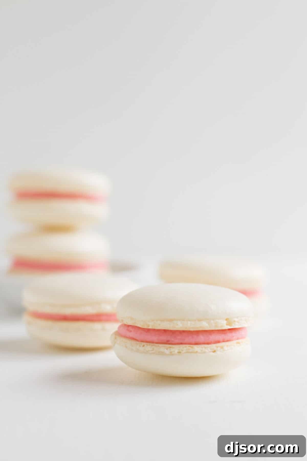 Strawberry Colada Macarons - Coconut French macarons are sandwiched with strawberry buttercream in these light meringue cookies. A perfectly smooth, white macaron shell, filled generously with light pink strawberry buttercream, showcasing the delicate 'feet' of the macaron.