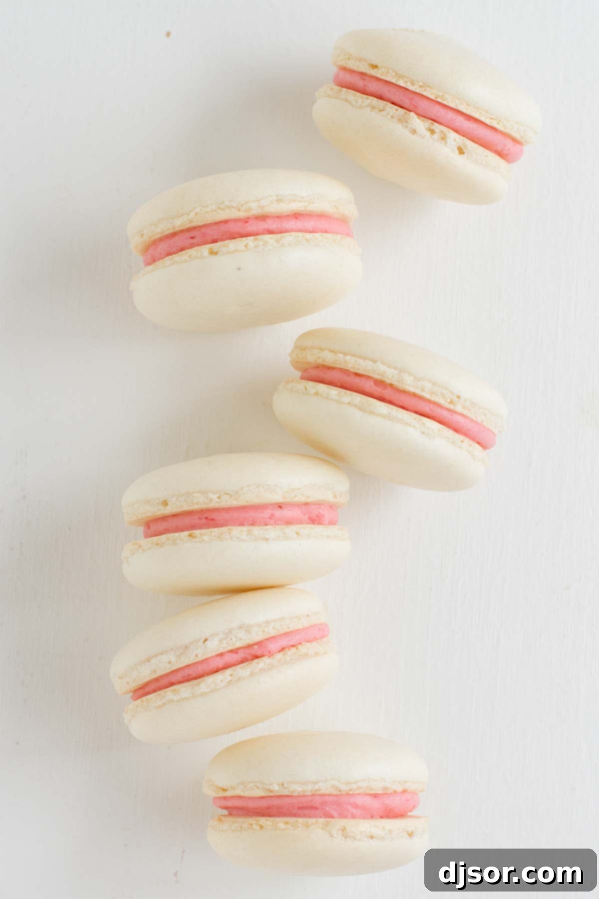 Strawberry Colada Macarons - Coconut French macarons are sandwiched with strawberry buttercream in these light meringue cookies. Strawberry Colada Macarons arranged on their sides, clearly displaying the generous layer of vibrant strawberry buttercream filling between the delicate coconut meringue shells.