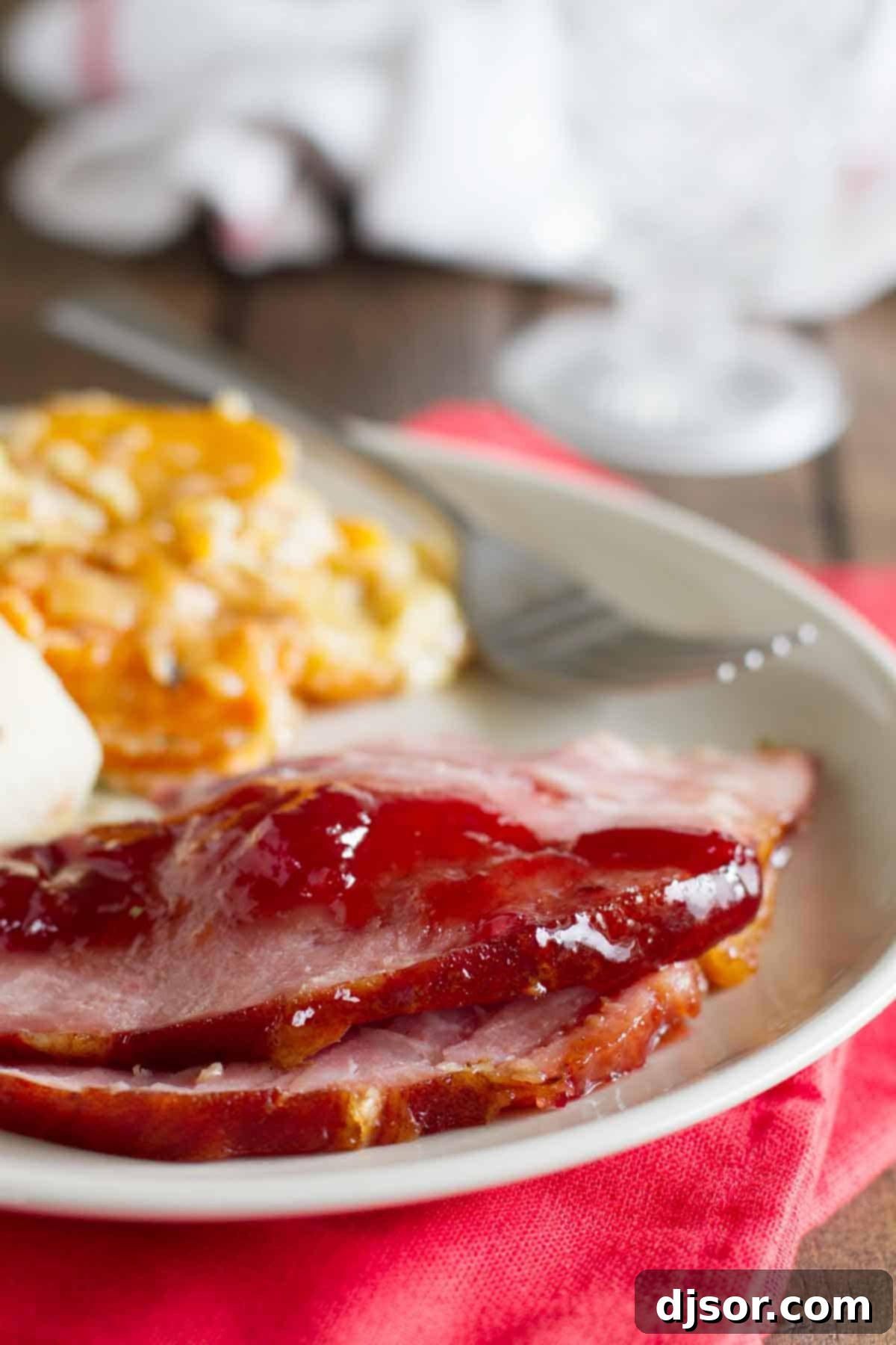 Close-up of succulent slices of Brown Sugar and Cherry Glazed Ham on a plate, surrounded by complementary holiday side dishes, showcasing its juicy texture and vibrant glaze.