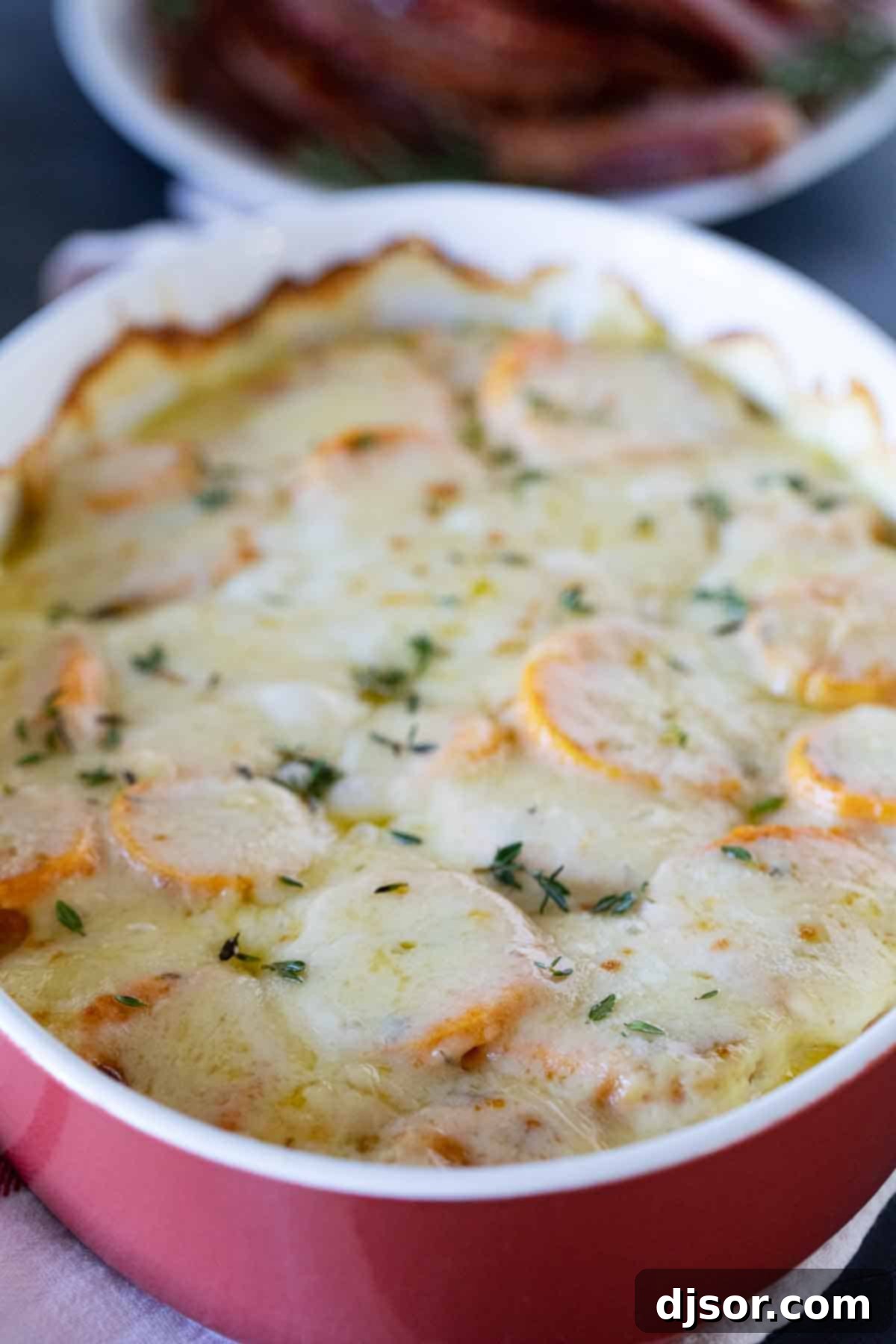 Creamy and cheesy, these Scalloped Sweet Potatoes are an easy addition to any holiday table. Layers or slice sweet potatoes are covered in cream and cheese in this indulgent savory side dish. A full baking dish of golden-brown Scalloped Sweet Potatoes, garnished with fresh thyme leaves.