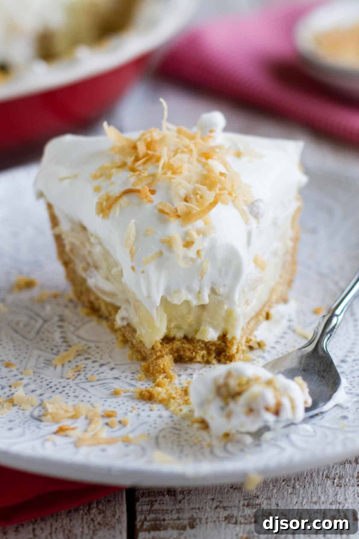 A delicious bite of Coconut Cream Pie showing the creamy filling, fluffy topping, and crisp cookie crust. fork taking a bite of coconut cream pie with a perfect crust
