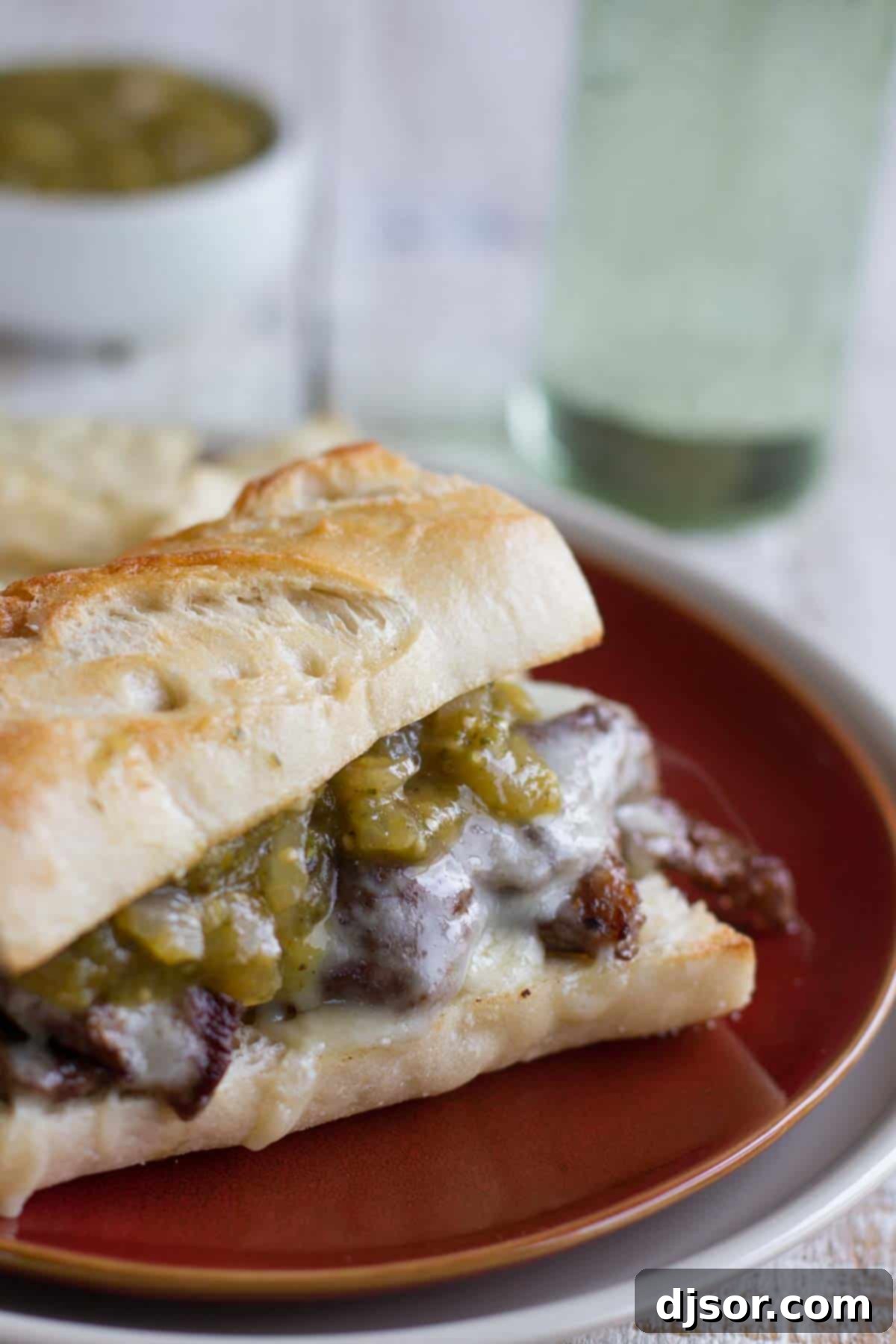 Hearty Salsa Verde Steak Sandwich A delicious Salsa Verde Steak Sandwich topped with perfectly cooked steak, melted cheese, and a generous drizzle of homemade salsa verde, presented on a plate.